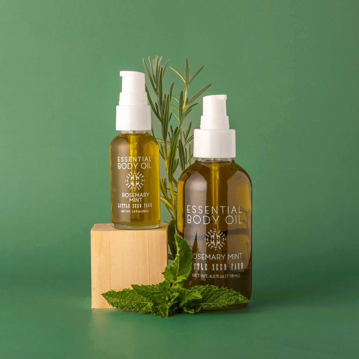 Little seed farms 1 ounce and 4 ounces rosemary mint body oils on a green background with mint and rosemary.