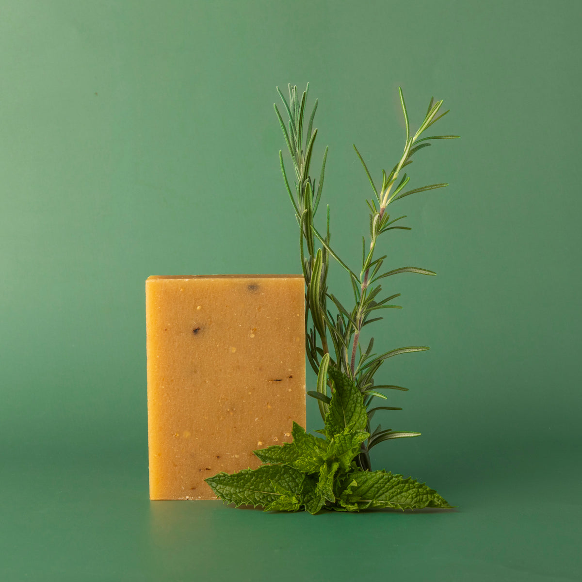 A bar of little seed farm rosemar mint goats milk soap on green background with rosemary and mint.