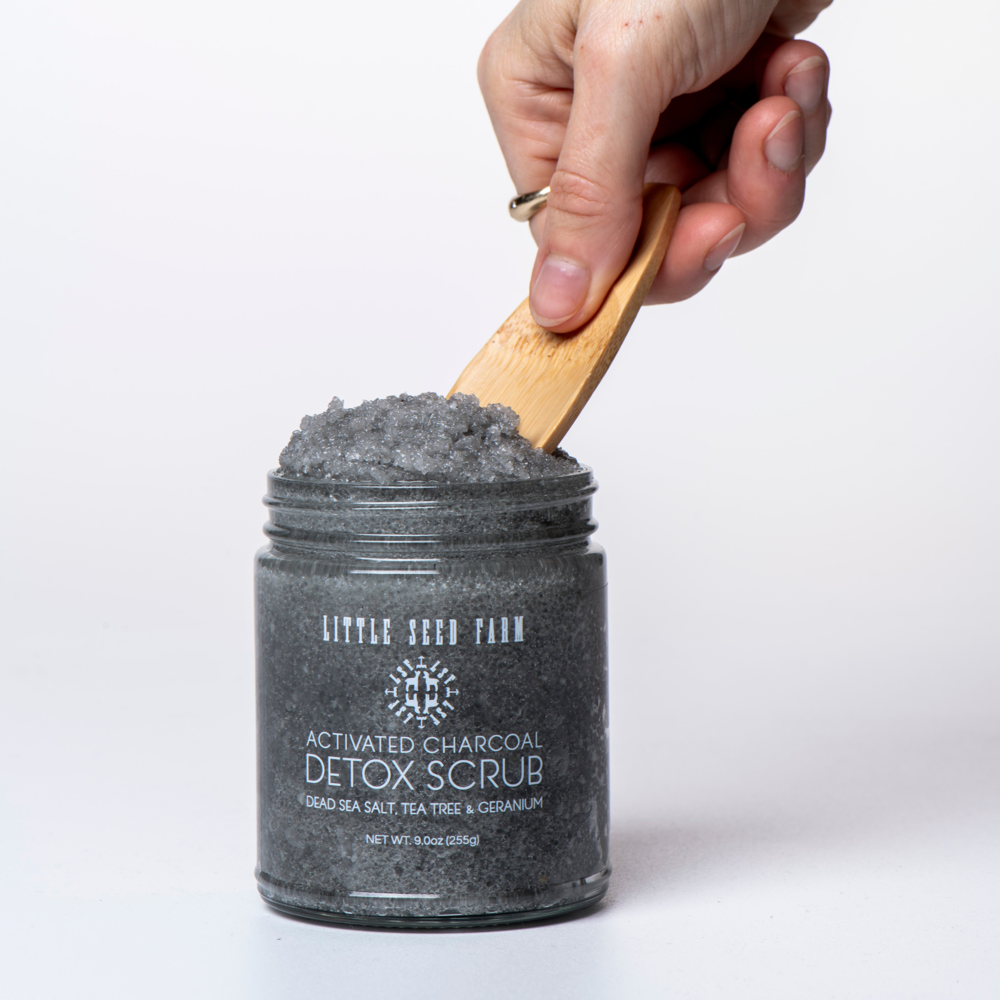 Jar of activated charcoal detox scrub with a wooden spoon on a white background
