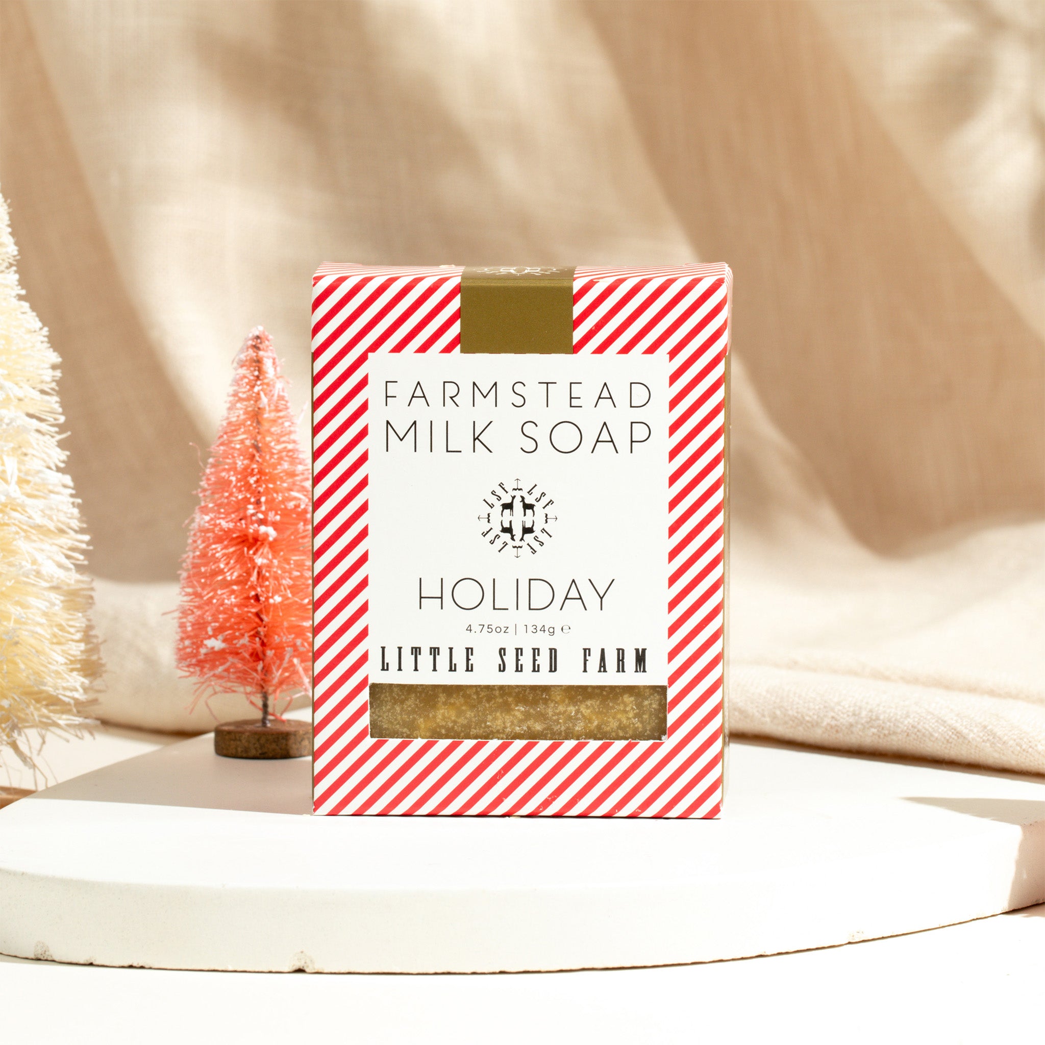 a bar of little seed farm holiday goats milk soap sitting next to some tiny fake Christmas trees.