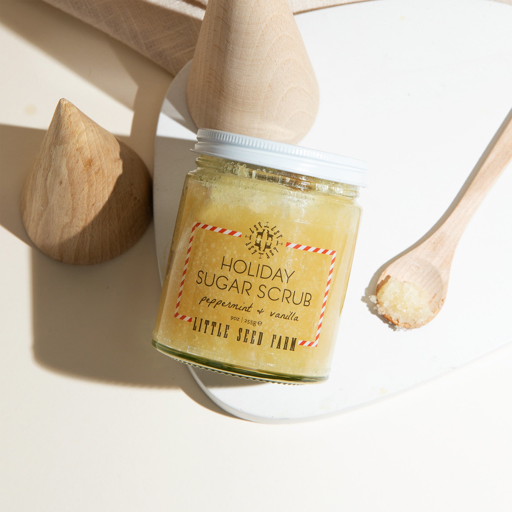 a jar of little seed farm holiday sugar scrub with a small spoon of it laying next to it.