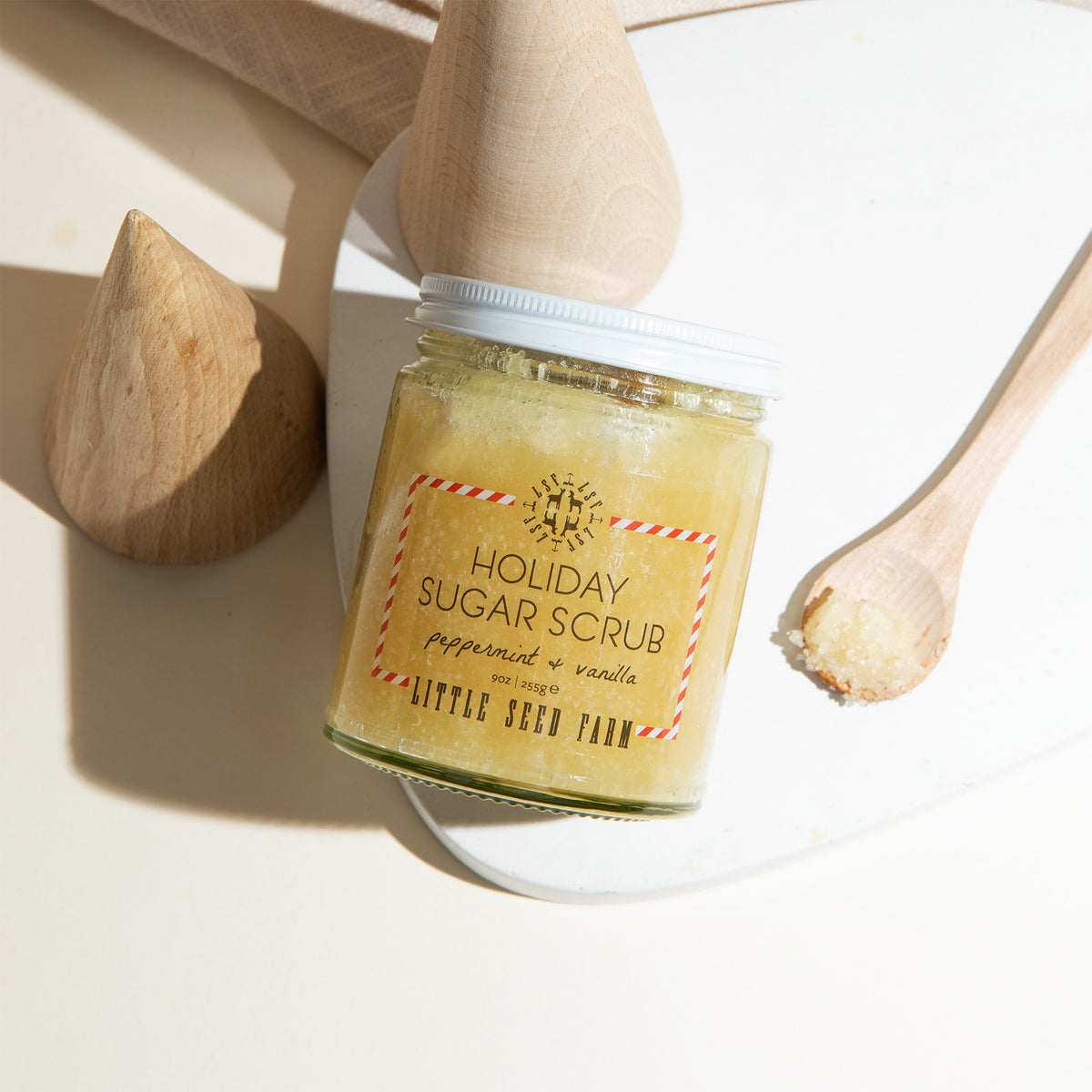 a jar of little seed farm holiday sugar scrub with a small spoon of it laying next to it.