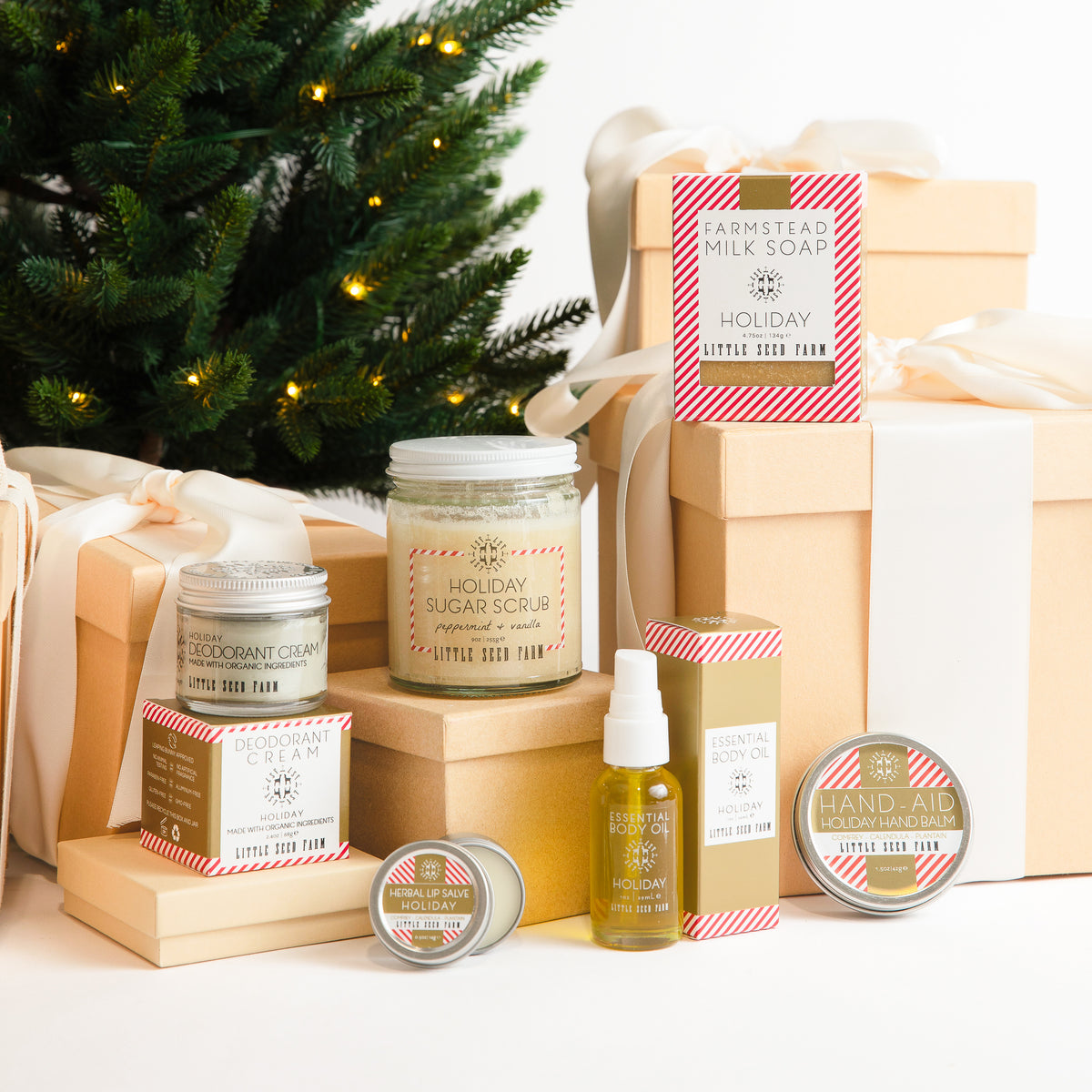 a group of all of the holiday scented products, including the deodorant, sugar scrub, herbal lip salve, body oil, hand aid and goats milk soap sitting on gift boxes.