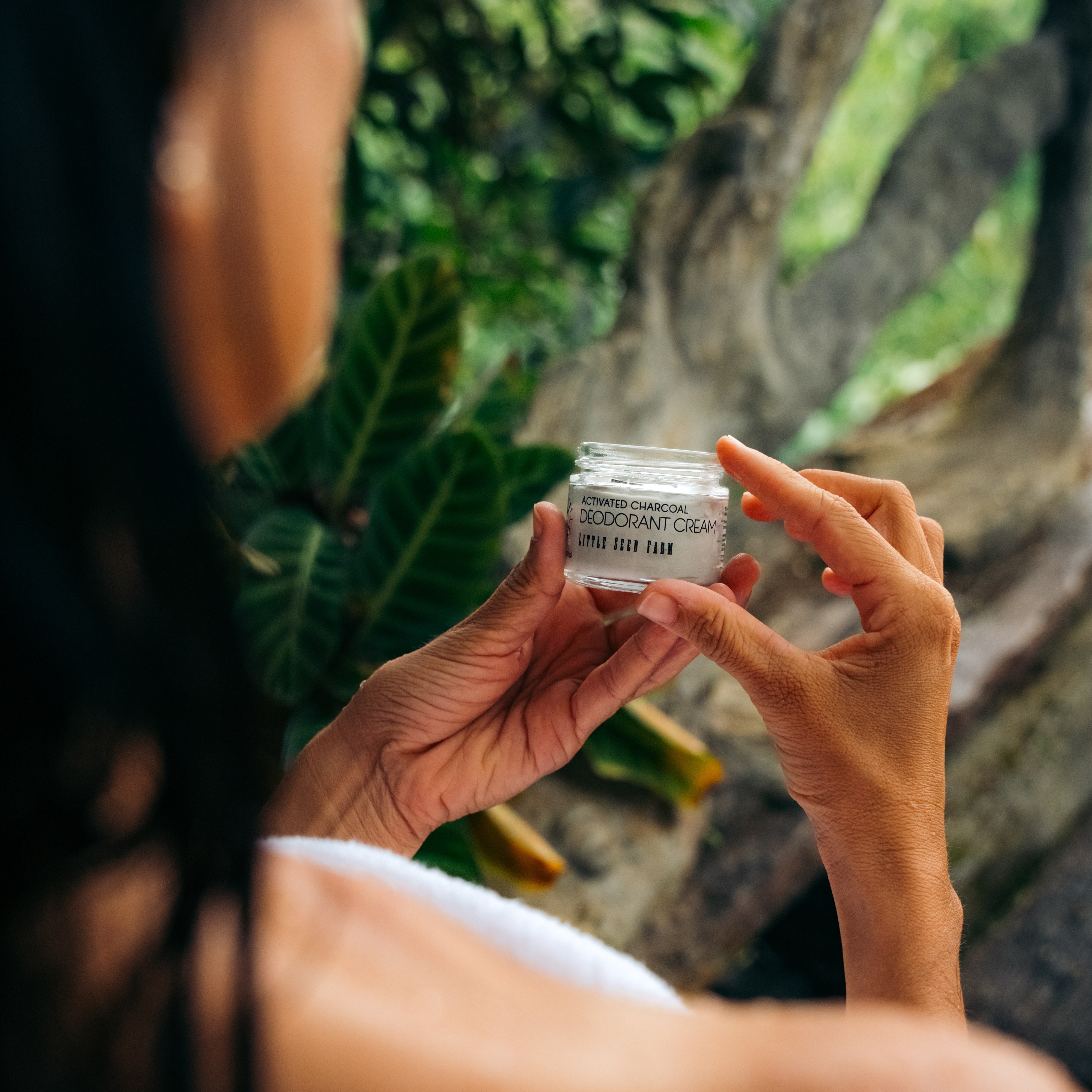 Person holding a jar of little seed farm natural deodorant cream with a natural background